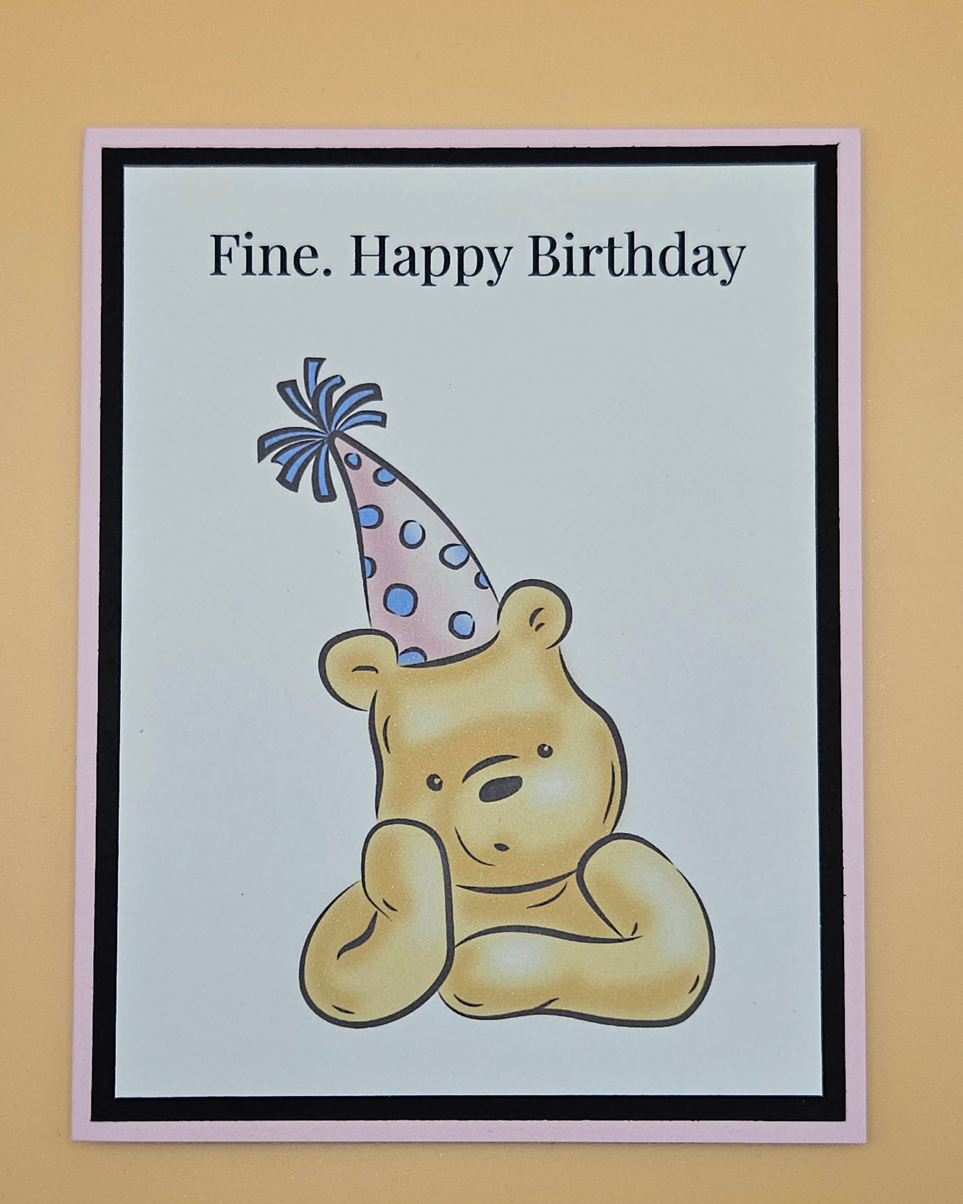 Handmade funny Winnie the Pooh birthday card with grumpy Pooh sitting arms crossed wearing a pink polka dot party hat on white inner panel with black and pink border. Text reads Fine Happy Birthday.