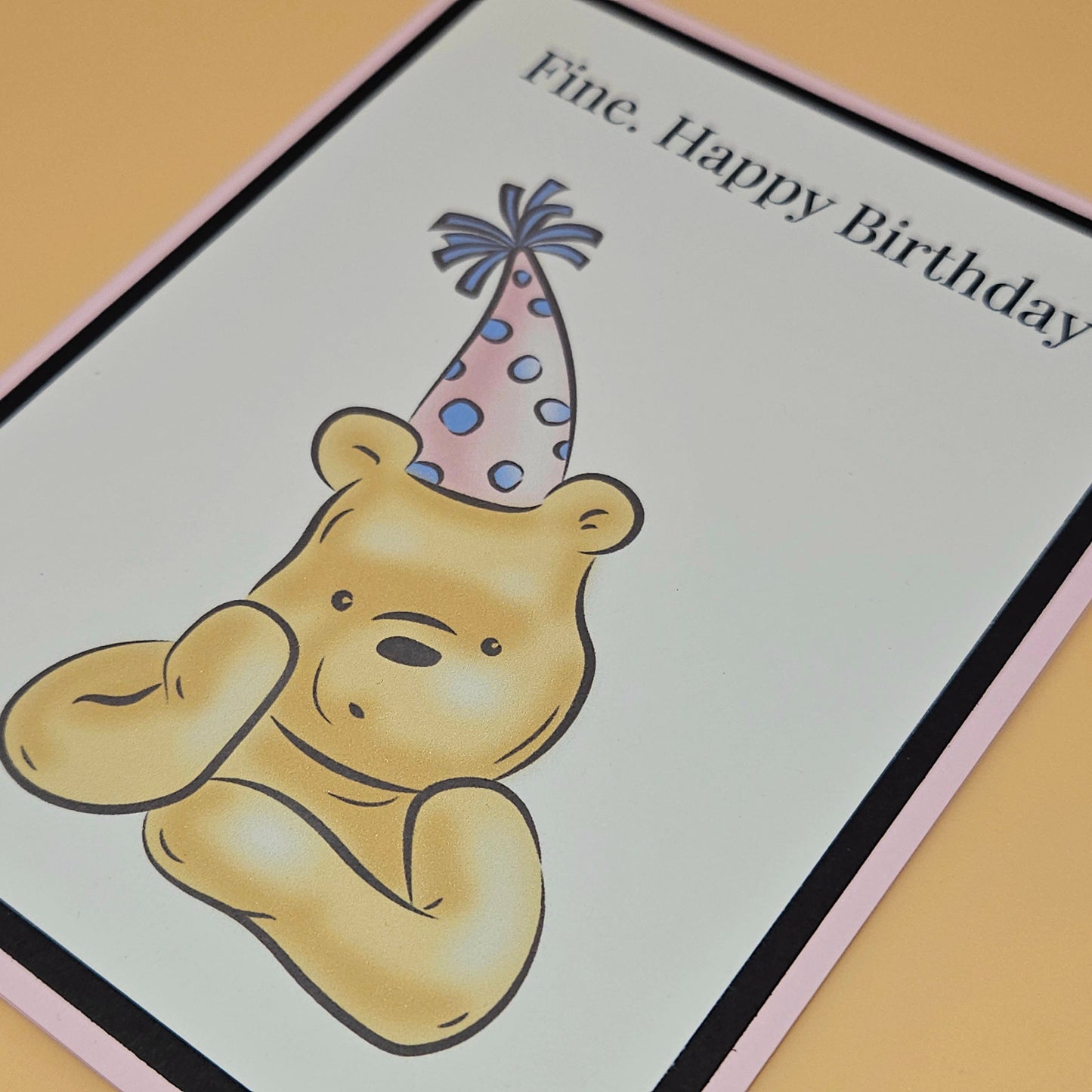 Handmade funny Winnie the Pooh birthday card with grumpy Pooh sitting arms crossed wearing a pink polka dot party hat on white inner panel with black and pink border. Text reads Fine Happy Birthday.