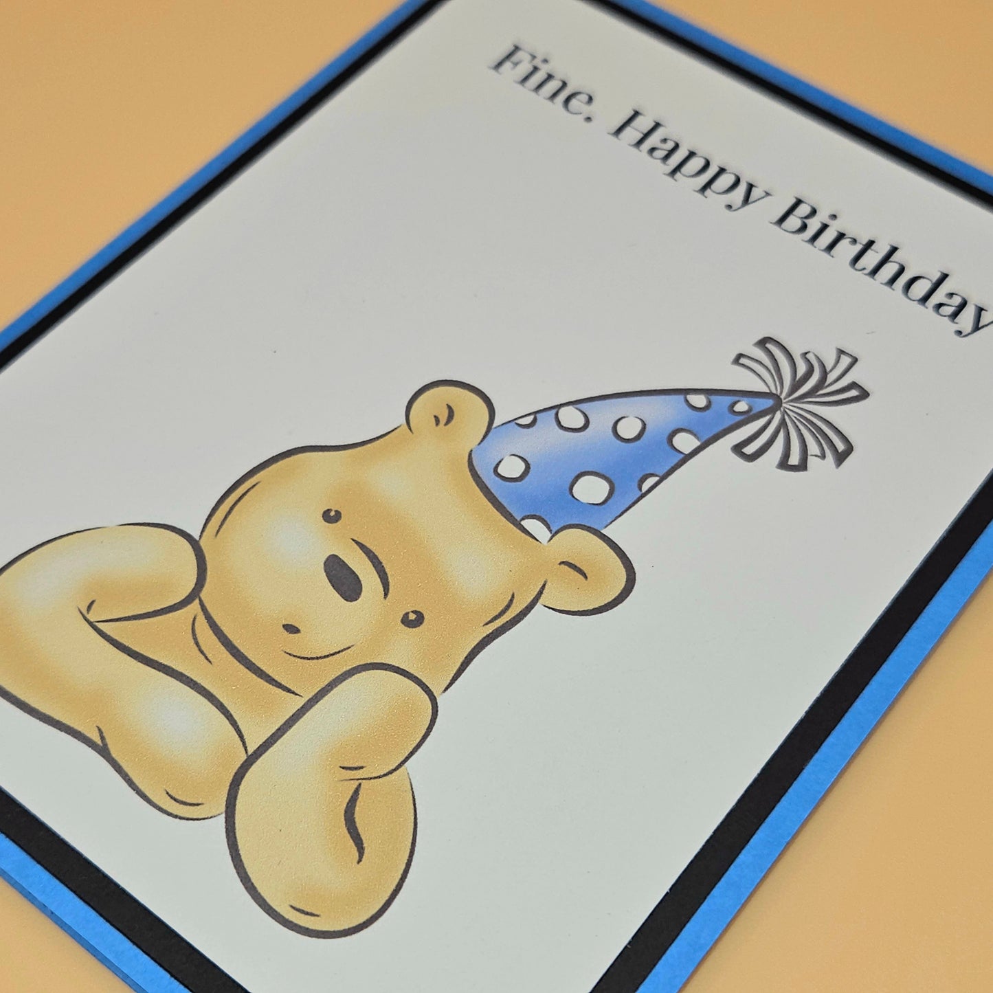 Handmade funny Winnie the Pooh birthday card with grumpy Pooh sitting arms crossed wearing a blue polka dot party hat on white inner panel with black and blue border. Text reads Fine Happy Birthday.