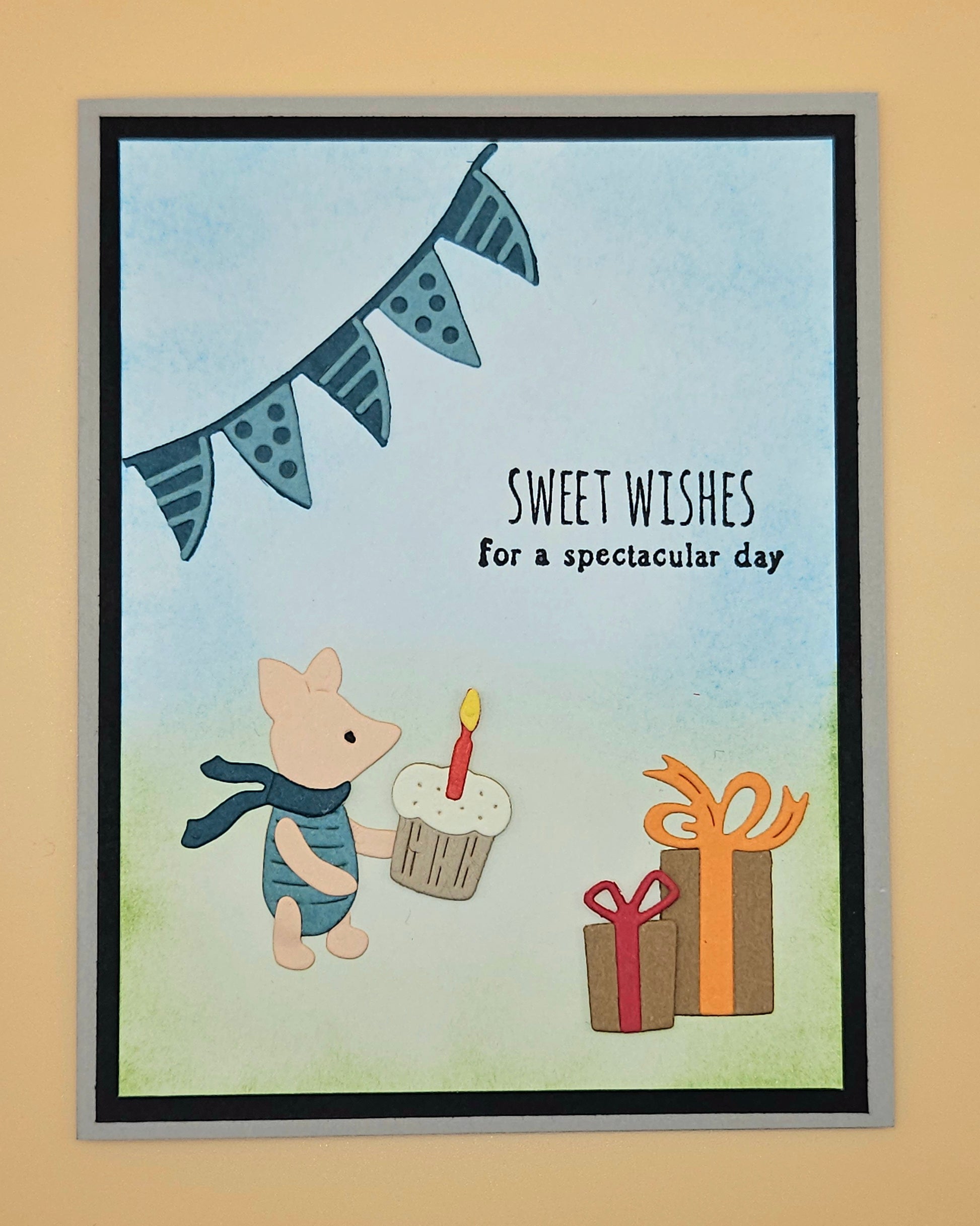 Handmade die-cut Winnie the Pooh birthday card with Piglet holding a cupcake under a bunting banner and gift boxes on light blue and green background. Text reads Sweet Wishes for a spectacular day.