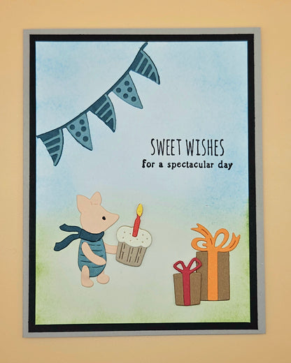 Handmade die-cut Winnie the Pooh birthday card with Piglet holding a cupcake under a bunting banner and gift boxes on light blue and green background. Text reads Sweet Wishes for a spectacular day.