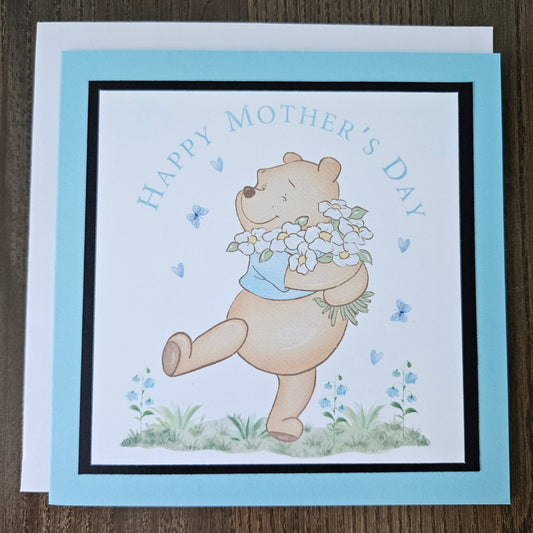Mother's Day card with a bear holding flowers on a wooden surface