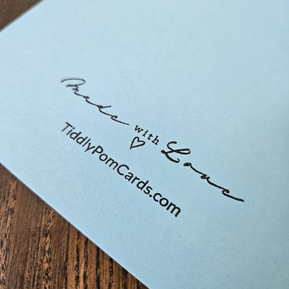 Light blue card with 'Made with Love' text and a heart symbol, on a wooden surface.