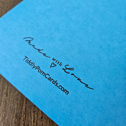 Blue card with 'Made with Love' and 'TiddlyPomCards.com' text on a wooden surface