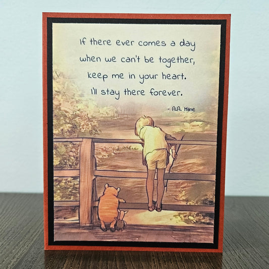 handmade vertical A2 greeting card featuring a warm color storybook illustration of Winnie the Pooh, Christopher Robin, and Piglet standing on a wooden bridge, printed with the A.A. Milne quote about keeping someone in your heart forever, finished with a black mat and a rust orange outer card border.