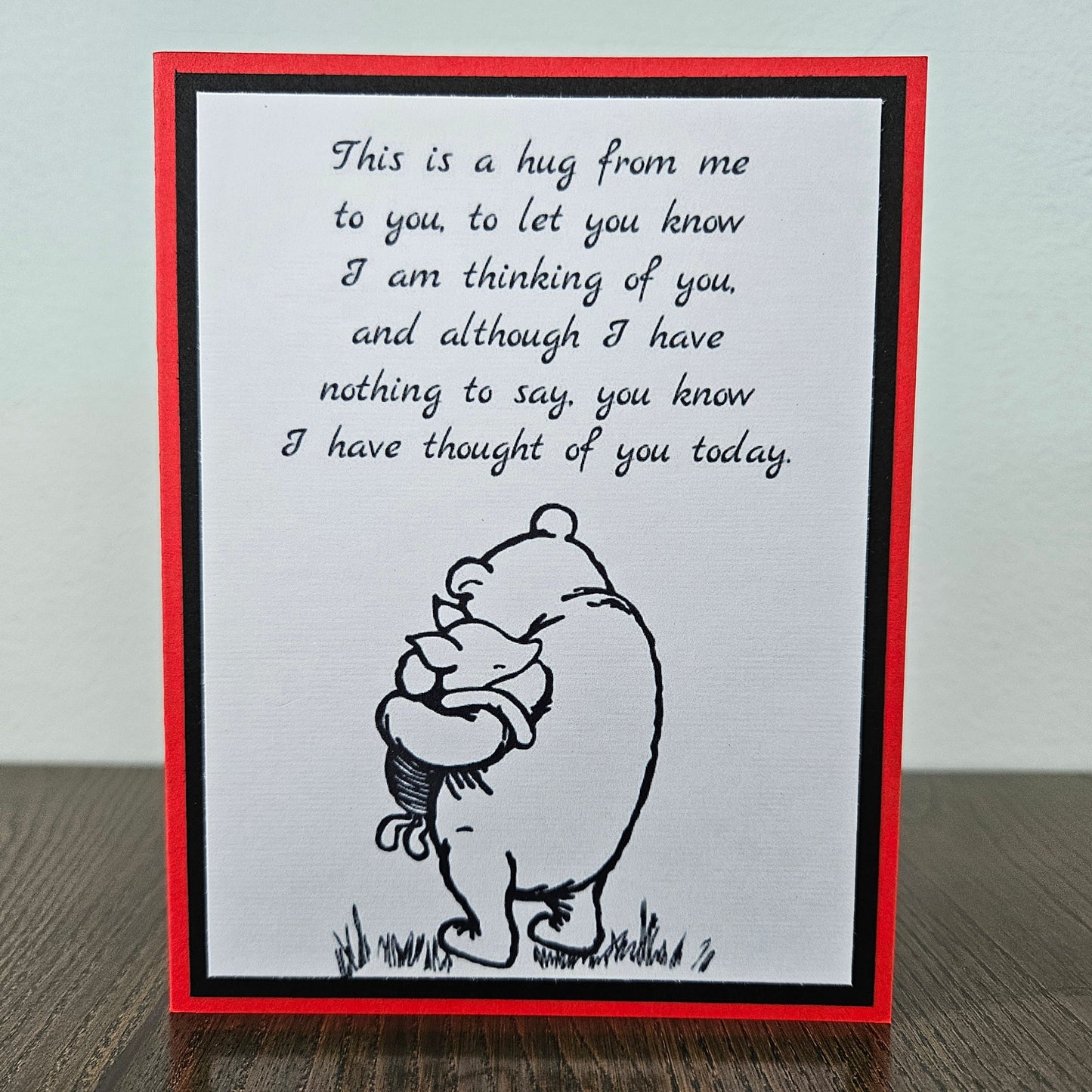 handmade A2 greeting card featuring a classic black ink sketch of Winnie the Pooh hugging Piglet, printed with a touching poem about sending a hug to show someone they are being thought of, framed with a bold black mat and a vibrant red card border.
