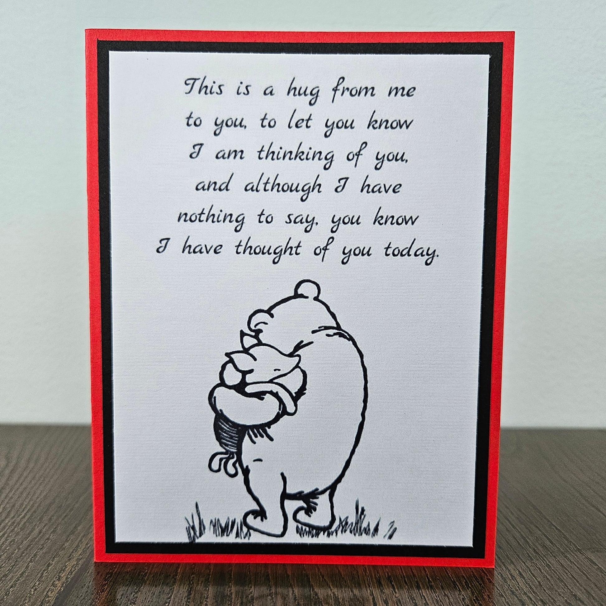 handmade A2 greeting card featuring a classic black ink sketch of Winnie the Pooh hugging Piglet, printed with a touching poem about sending a hug to show someone they are being thought of, framed with a bold black mat and a vibrant red card border.