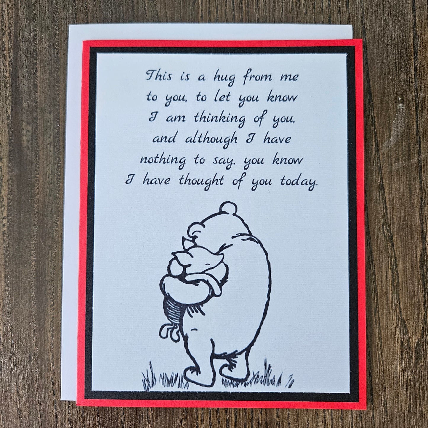 handmade A2 greeting card featuring a classic black ink sketch of Winnie the Pooh hugging Piglet, printed with a touching poem about sending a hug to show someone they are being thought of, framed with a bold black mat and a vibrant red card border.