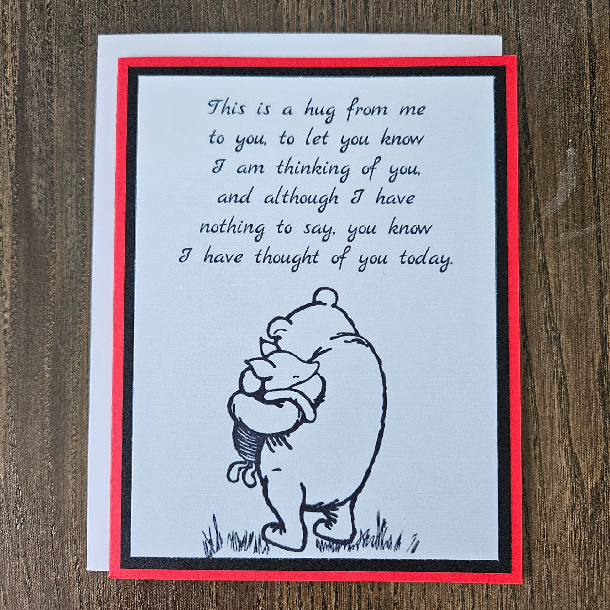 handmade A2 greeting card featuring a classic black ink sketch of Winnie the Pooh hugging Piglet, printed with a touching poem about sending a hug to show someone they are being thought of, framed with a bold black mat and a vibrant red card border.