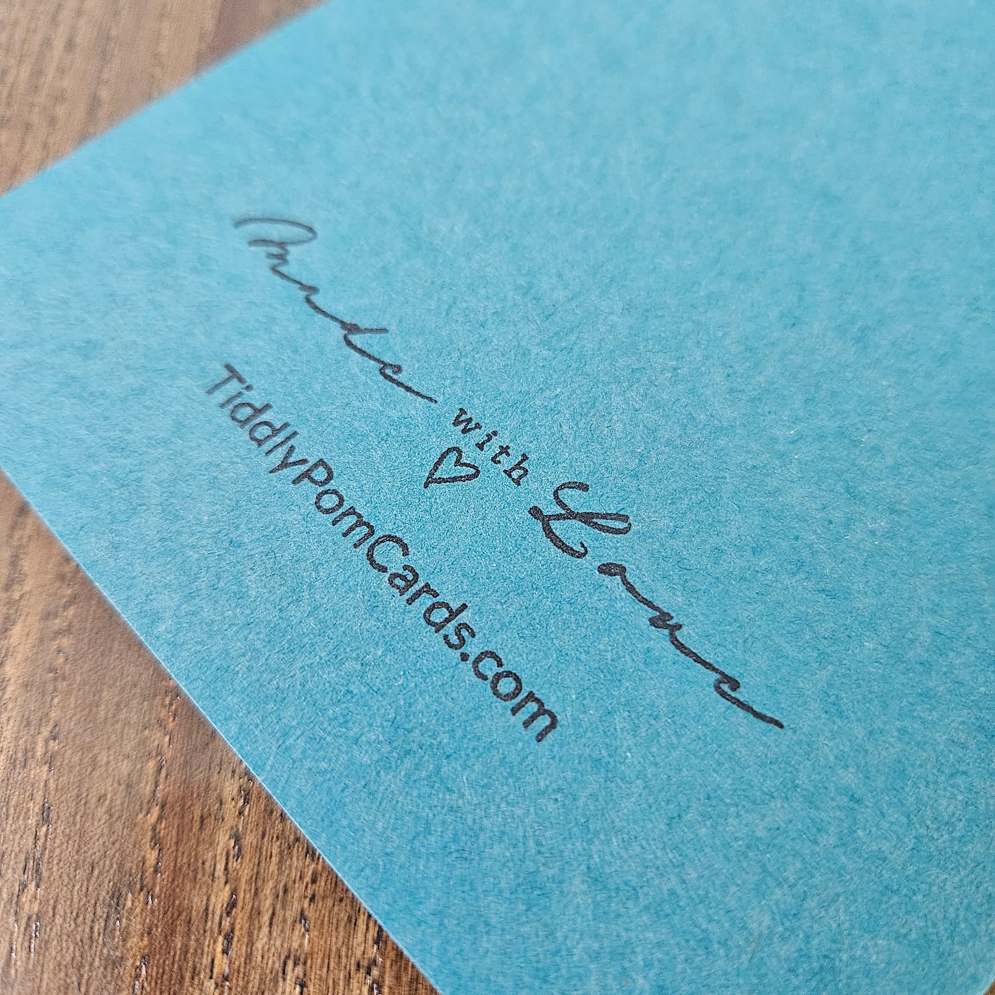 Blue card with 'Made with Love' and 'TiddlyPomCards.com' text on a wooden surface