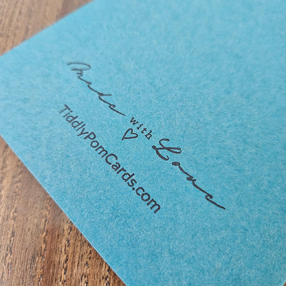 Blue card with 'Made with Love' and 'TiddlyPomCards.com' text on a wooden surface