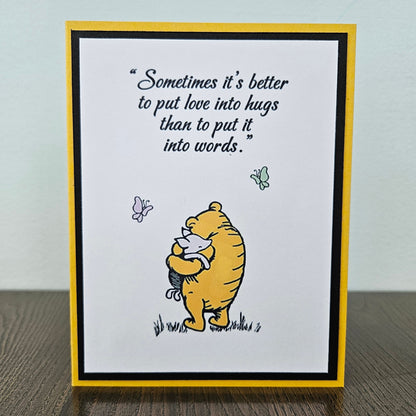 Card with Winnie the Pooh hugging a bear and a quote about love and hugs on a beige background.