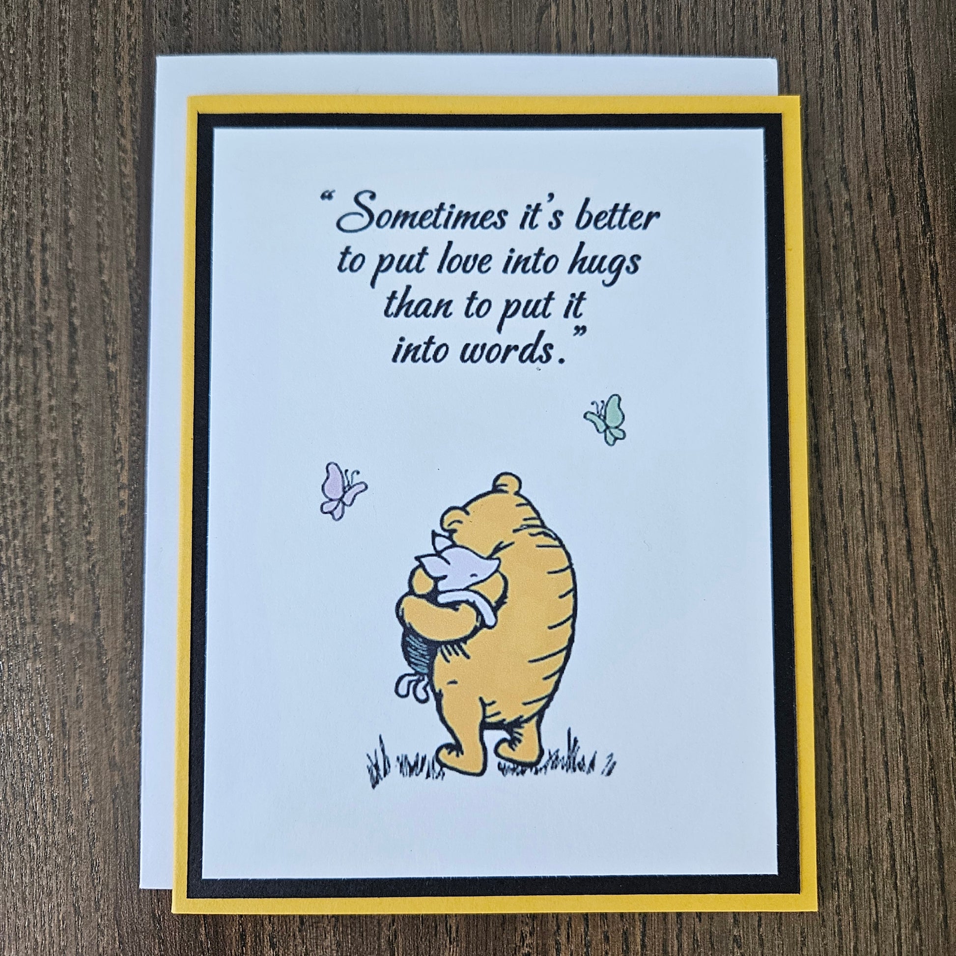 Card with Winnie the Pooh hugging a bear and a quote about love and hugs on a beige background.