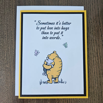 Card with Winnie the Pooh hugging a bear and a quote about love and hugs on a beige background.
