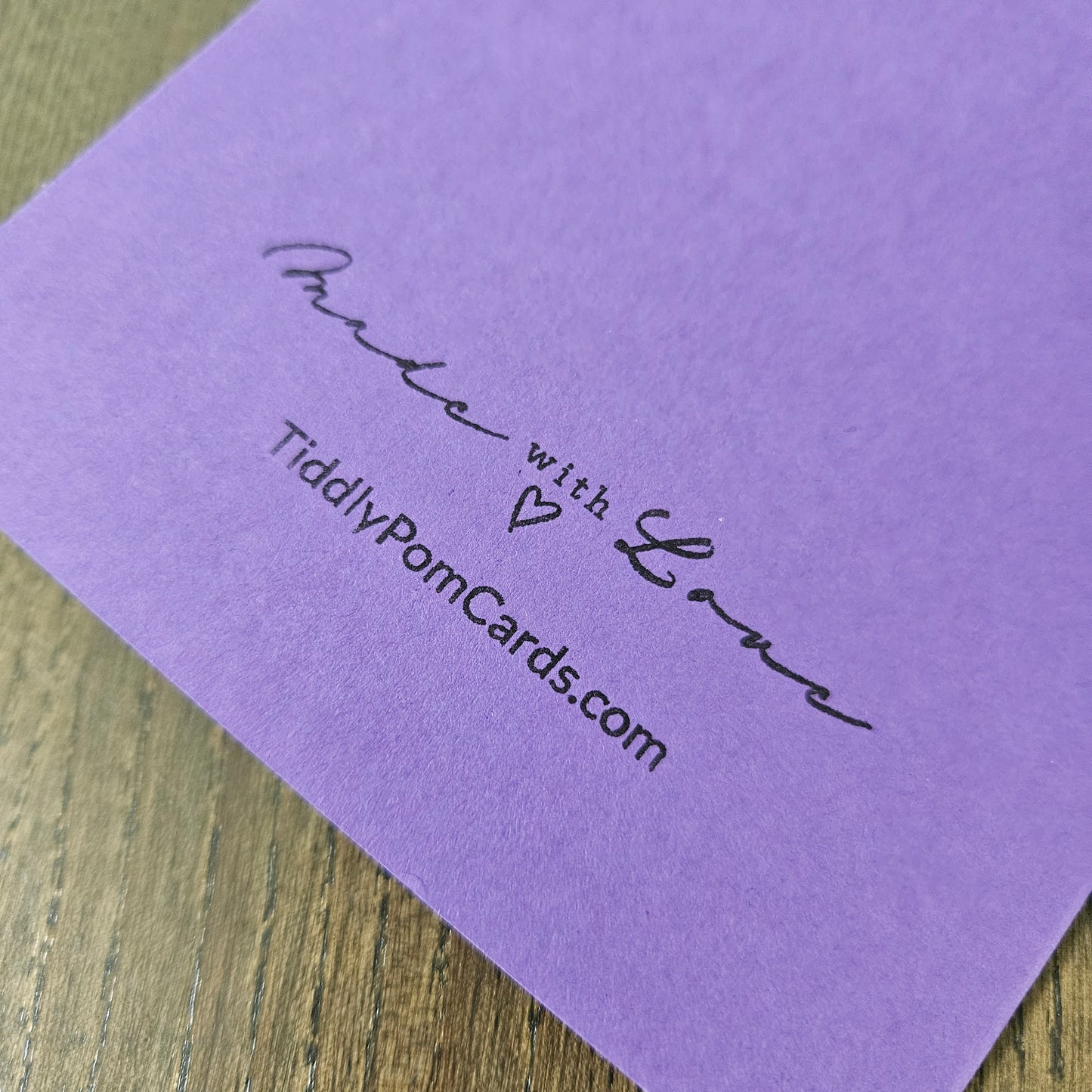 Purple card with 'Made with Love' text and website address on a wooden surface