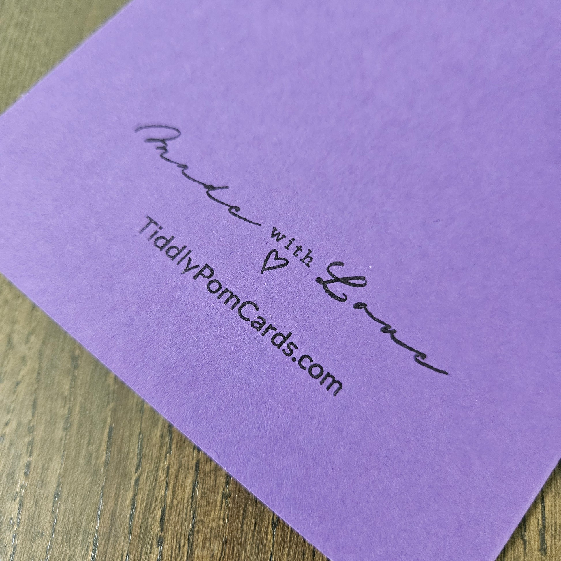 Purple card with 'Made with Love' text and website address on a wooden surface