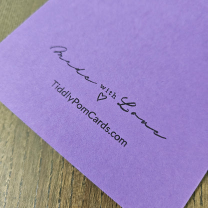 Purple card with 'Made with Love' text and website address on a wooden surface