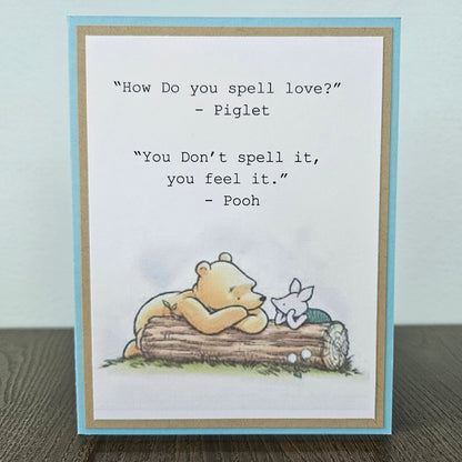 a handmade A2 friendship card featuring a classic storybook sketch illustration of Winnie the Pooh and Piglet walking together, printed with the iconic quote about how love is felt rather than spelled, finished with layered cardstock mat frames.