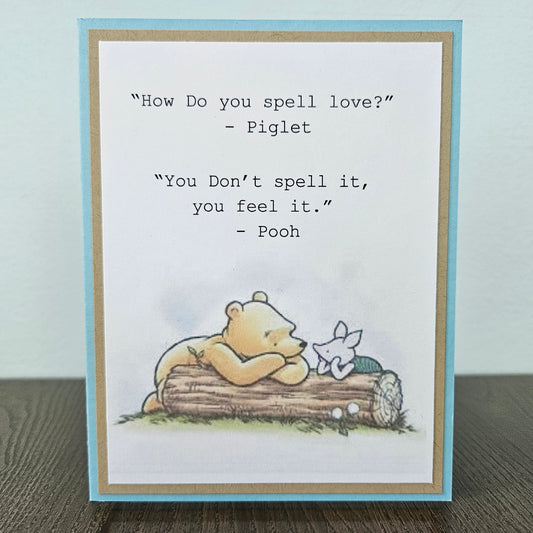 a handmade A2 friendship card featuring a classic storybook sketch illustration of Winnie the Pooh and Piglet walking together, printed with the iconic quote about how love is felt rather than spelled, finished with layered cardstock mat frames.