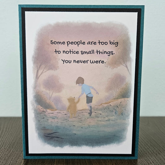 Front of a handmade A2 greeting card featuring a soft watercolor illustration of Winnie the Pooh and Christopher Robin walking together, printed with the quote Some people are too big to notice small things. You never were, finished with a crisp black mat and a rich teal card border.