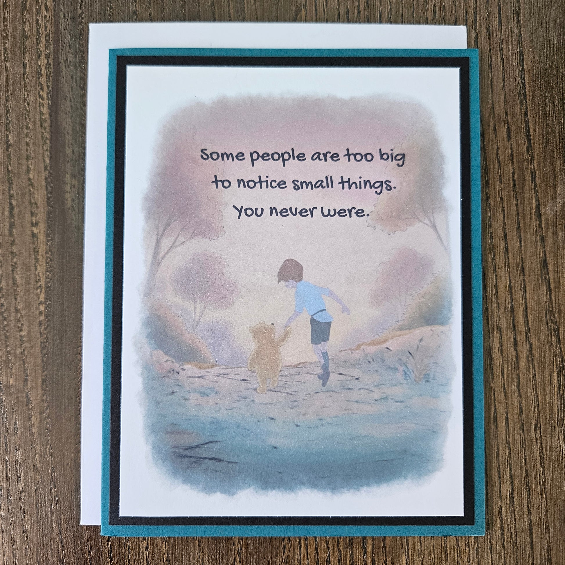 Front of a handmade A2 greeting card featuring a soft watercolor illustration of Winnie the Pooh and Christopher Robin walking together, printed with the quote Some people are too big to notice small things. You never were, finished with a crisp black mat and a rich teal card border.