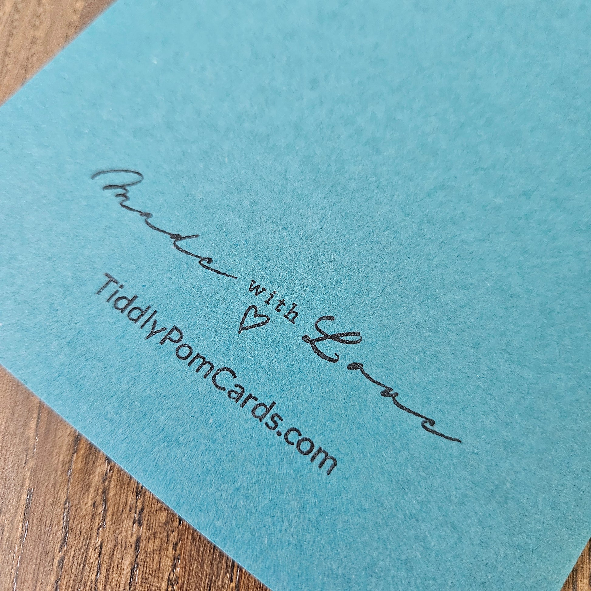 Blue card with 'Made with Love' and 'TiddlyPomCards.com' text on a wooden surface