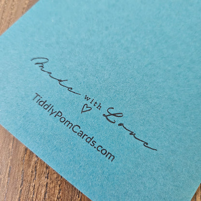 Blue card with 'Made with Love' and 'TiddlyPomCards.com' text on a wooden surface