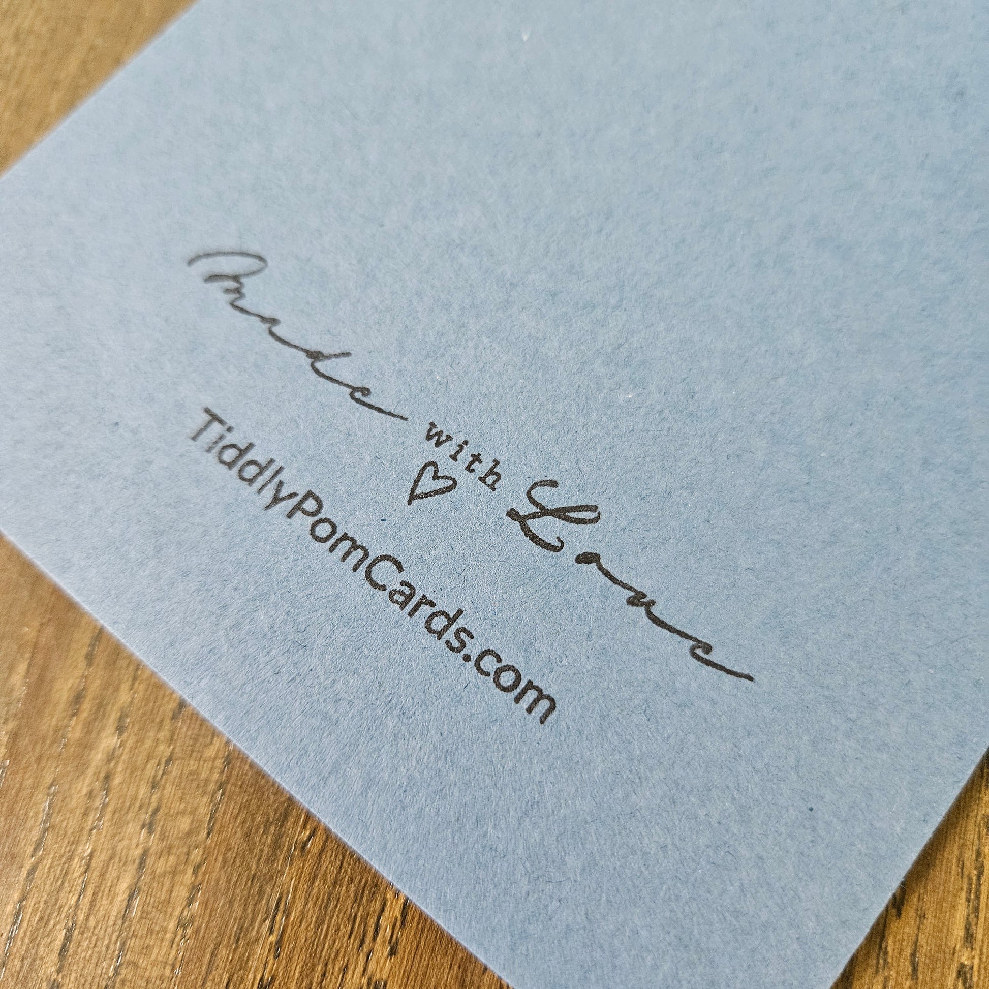 Light blue card with 'Made with Love' and TiddlyPomCards.com text on a wooden surface
