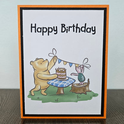 Birthday card with a bear and rabbit celebrating a birthday, featuring a cake and flags.