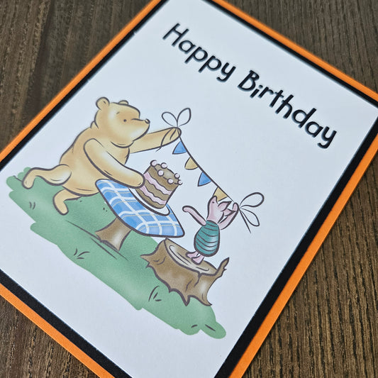 Birthday card with cartoon bear and rabbit design on a wooden surface