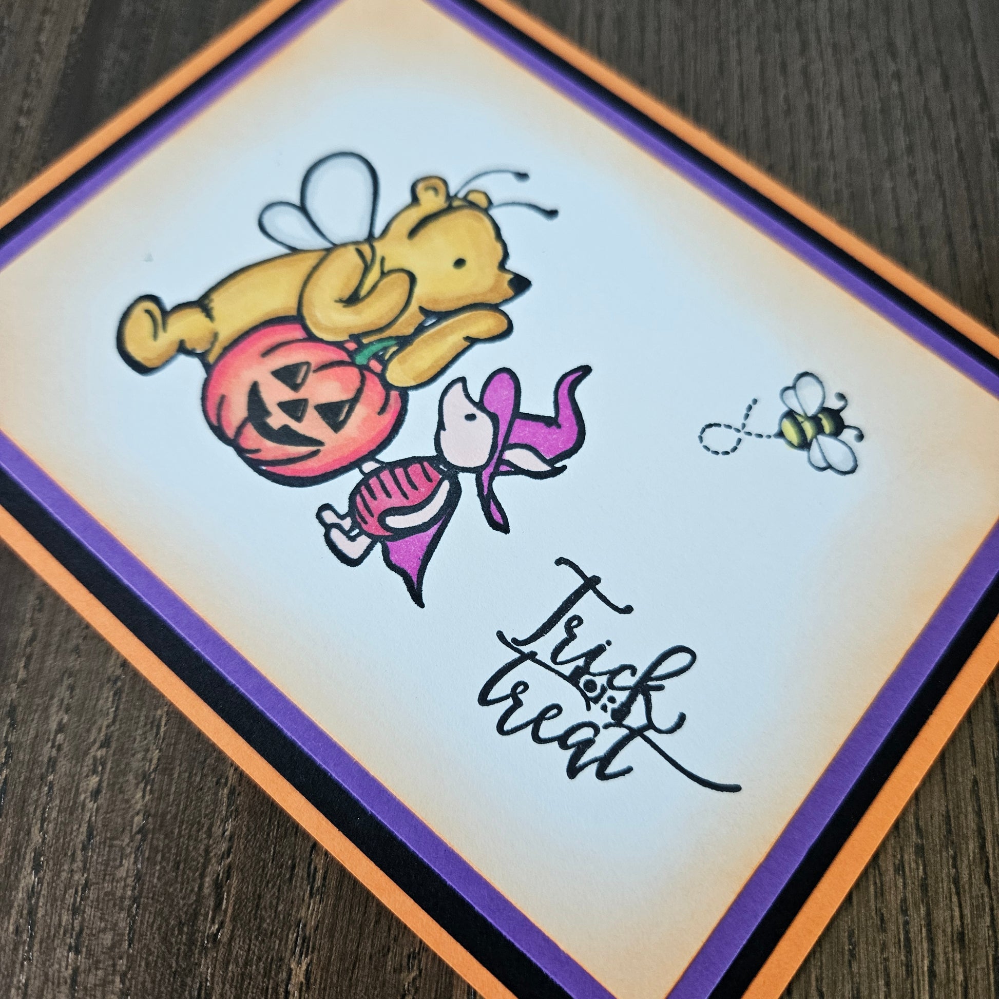 Halloween-themed card with a bear holding a pumpkin and a bee, on a wooden surface.