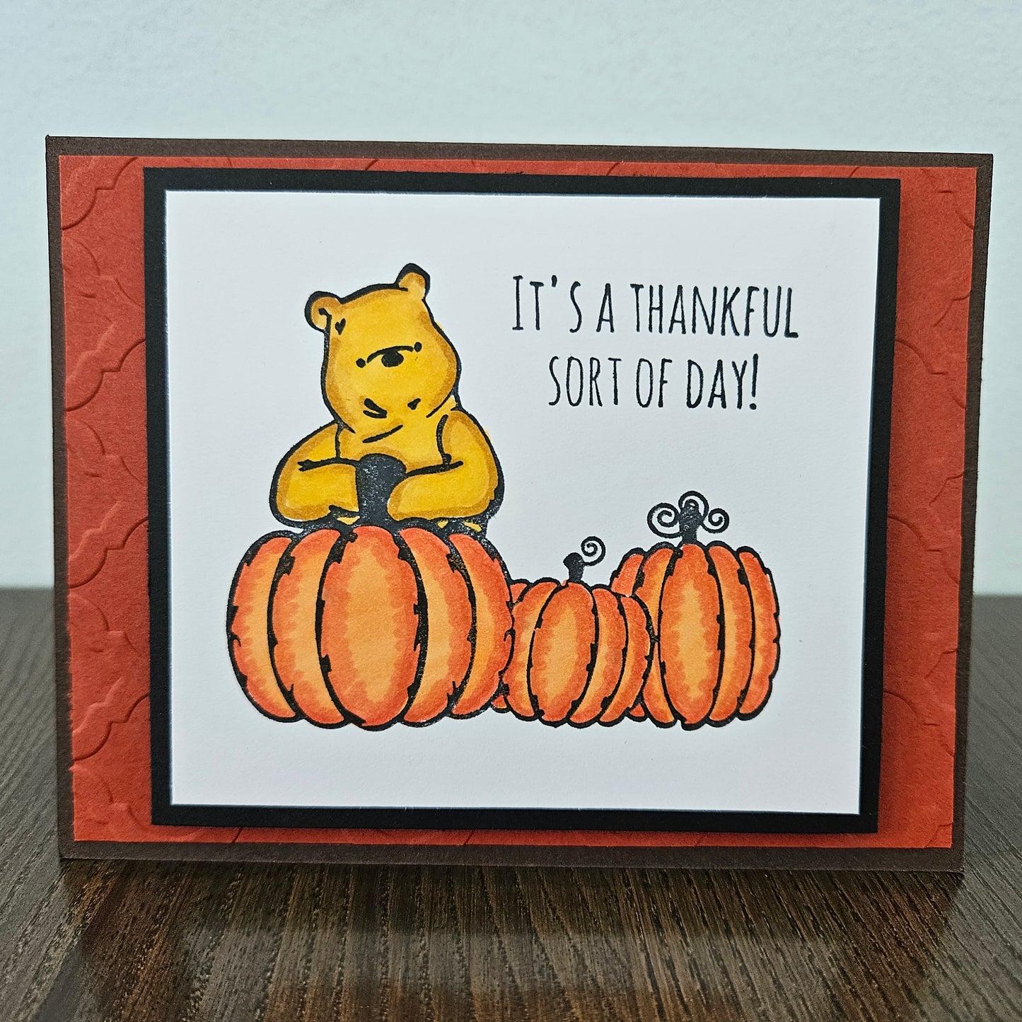 handmade horizontal A2 Thanksgiving card featuring classic Winnie the Pooh with three orange pumpkins on a white panel, an embossed textured orange mat, and a brown base, alongside views of the "HAPPY Thanksgiving" inside text and the branded back logo 