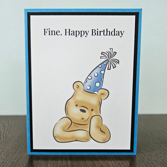 Handmade funny Winnie the Pooh birthday card for him featuring an illustration of a grumpy Pooh Bear wearing a party hat with arms crossed next to a text banner that reads Fine. Happy Birthday, set against a cornflower blue layered border.