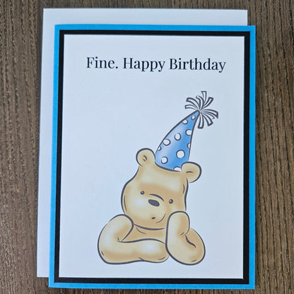Handmade funny Winnie the Pooh birthday card for him featuring an illustration of a grumpy Pooh Bear wearing a party hat with arms crossed next to a text banner that reads Fine. Happy Birthday, set against a cornflower blue layered border.