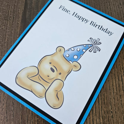 Birthday card with a teddy bear wearing a party hat on a wooden surface