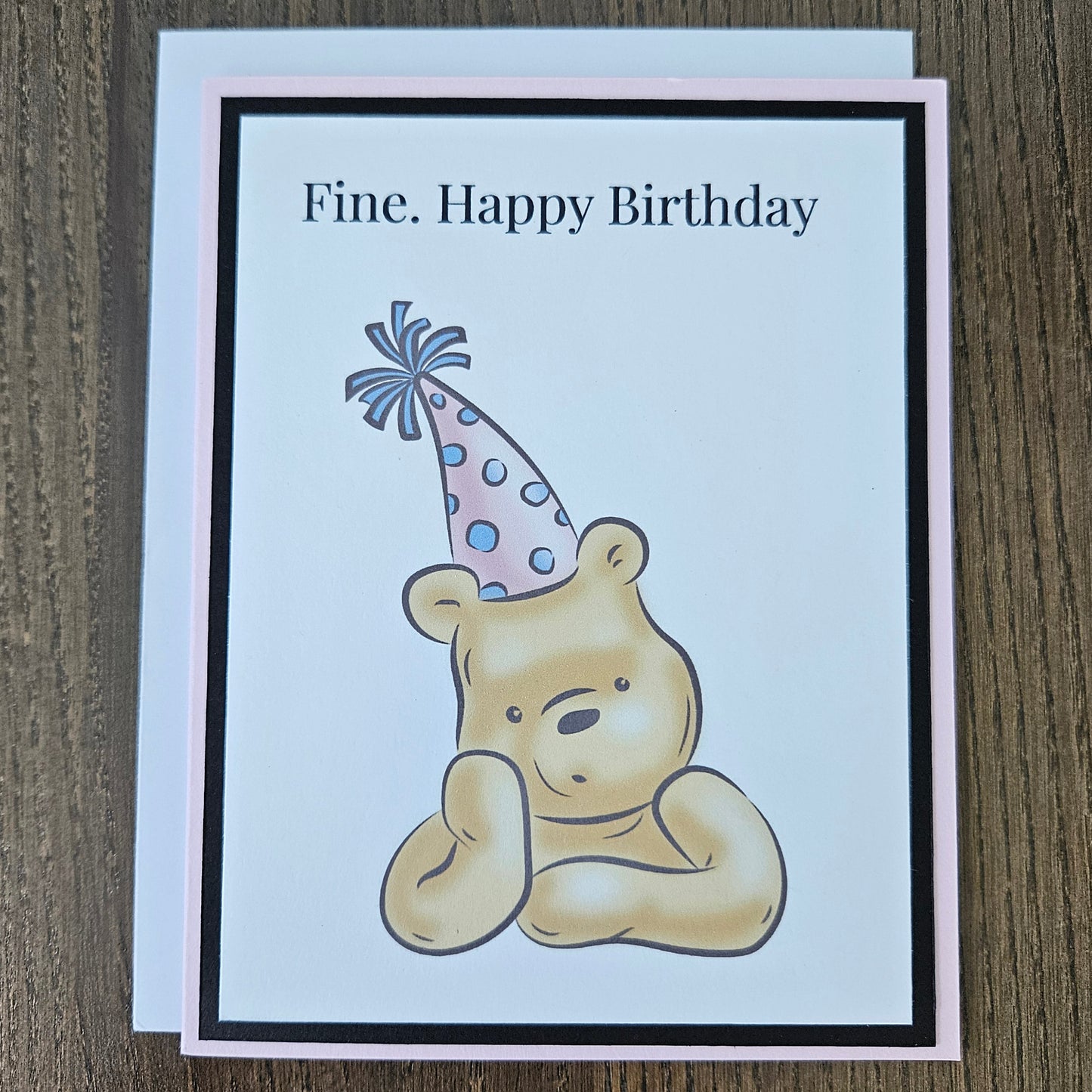 Birthday card with a bear holding a party hat on a wooden surface