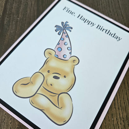 Birthday card with a bear holding a party hat on a wooden surface