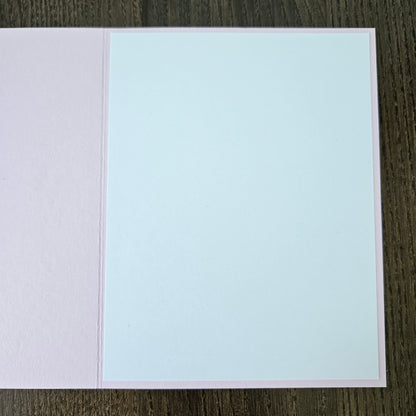 Two-tone light blue and pink card on a dark wooden surface