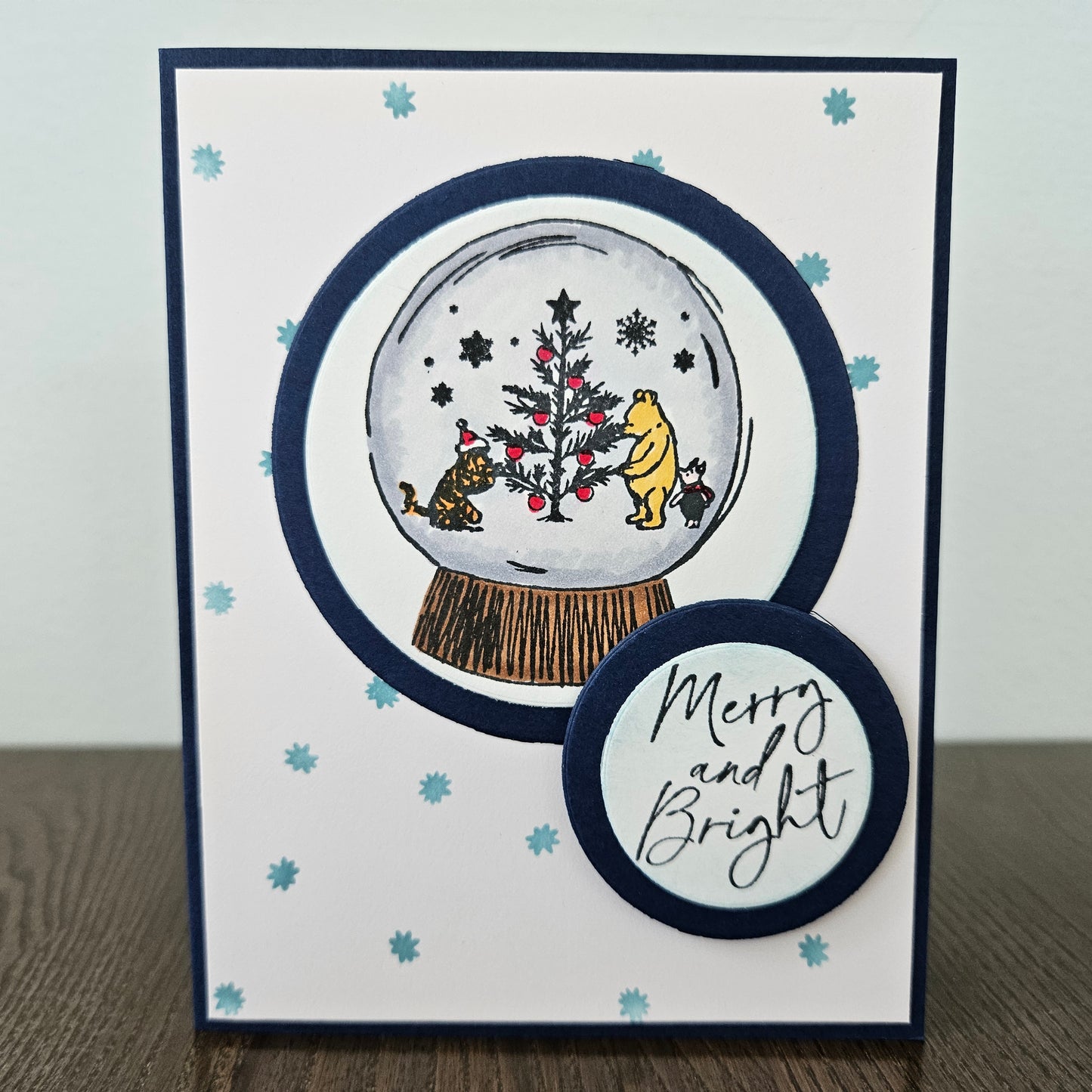 Christmas-themed card with a snow globe design featuring Winnie the Pooh and friends, on a white background.