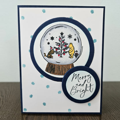 Christmas-themed card with a snow globe design featuring Winnie the Pooh and friends, on a white background.