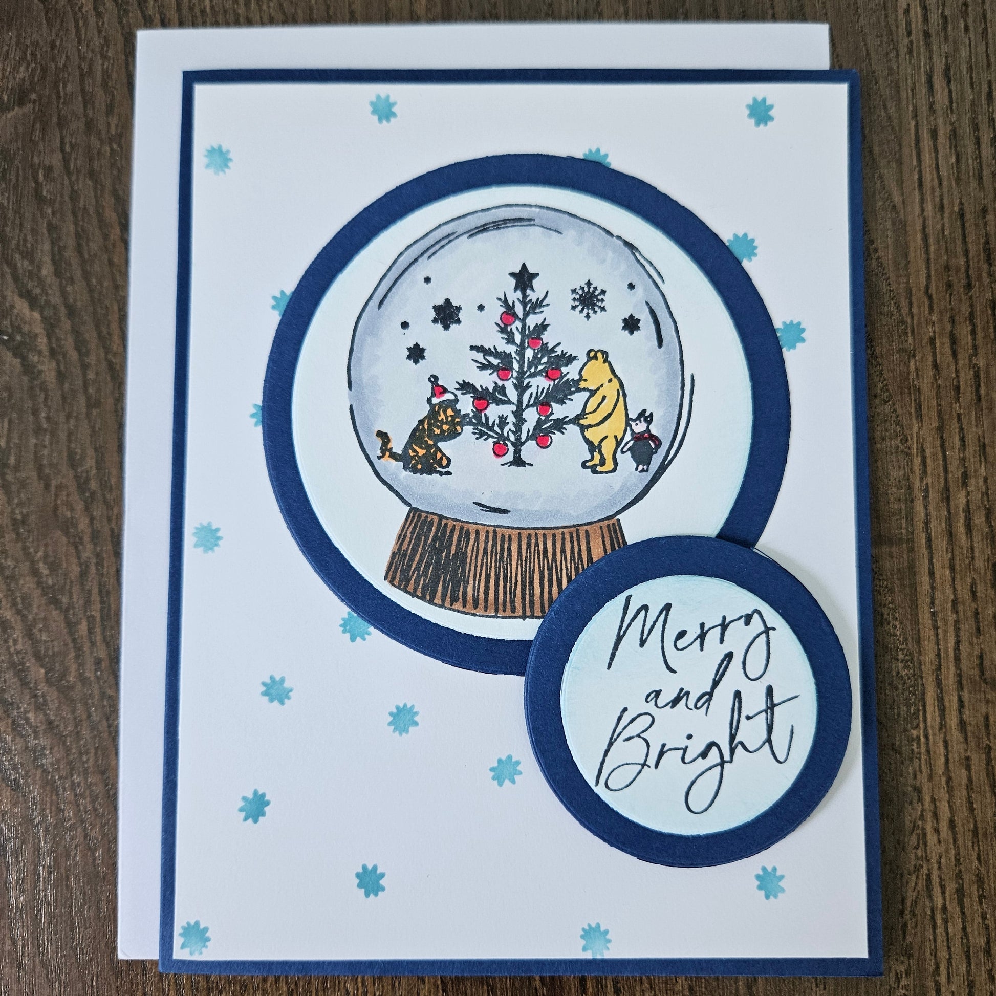 Christmas-themed card with snow globe design and 'Merry and Bright' text on a wooden surface.