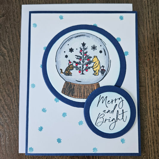 Christmas-themed card with snow globe design and 'Merry and Bright' text on a wooden surface.