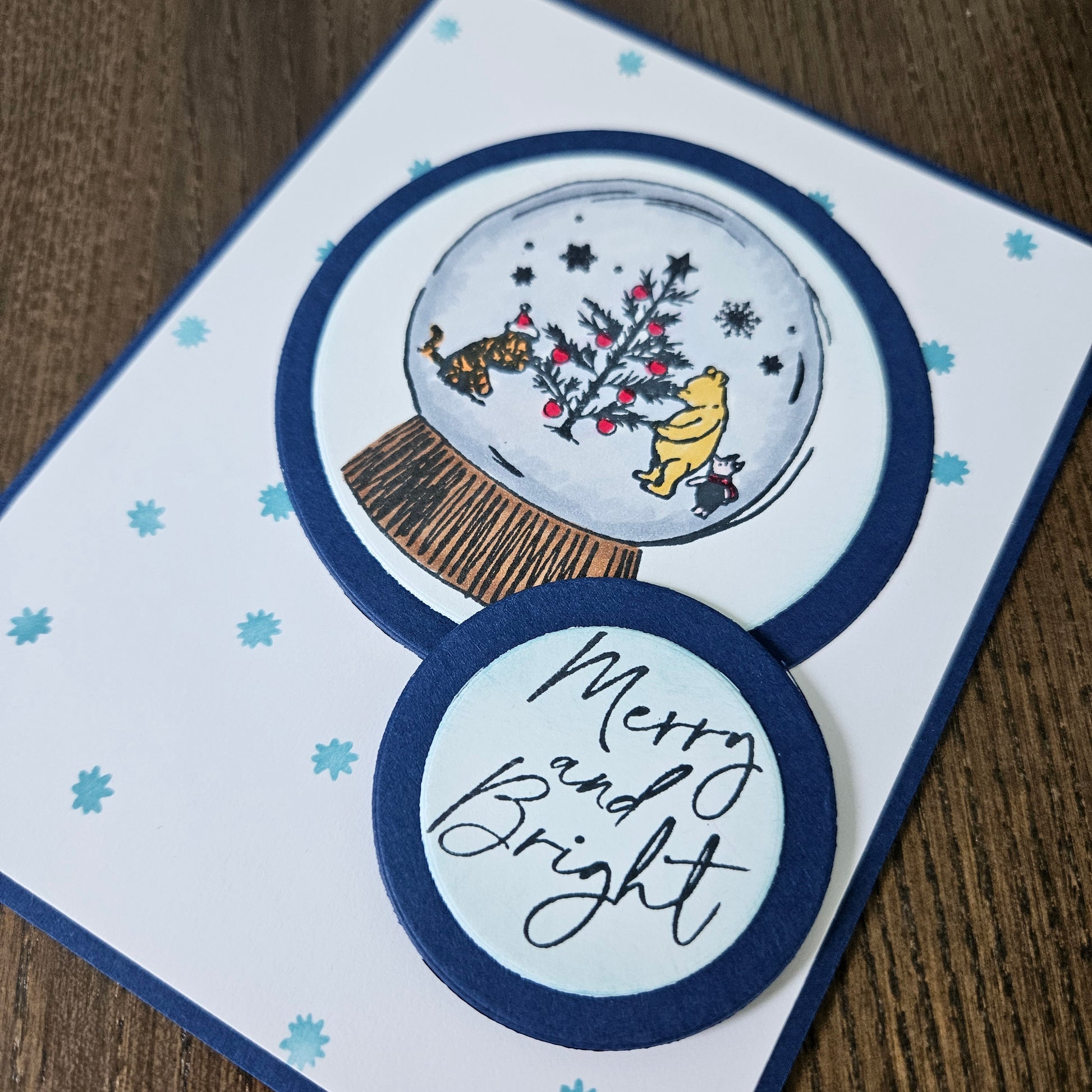 Christmas-themed card with snow globe illustration and 'Merry and Bright' text on a wooden surface.