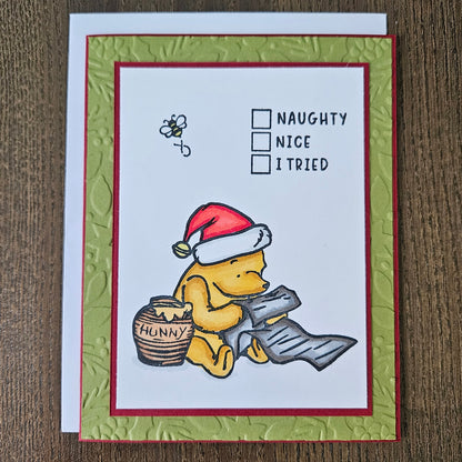 Handmade Winnie the Pooh Christmas card featuring a classic hand-colored illustration of Pooh Bear wearing a Santa hat and checking off I Tried on a Naughty or Nice checklist next to a hunny pot.