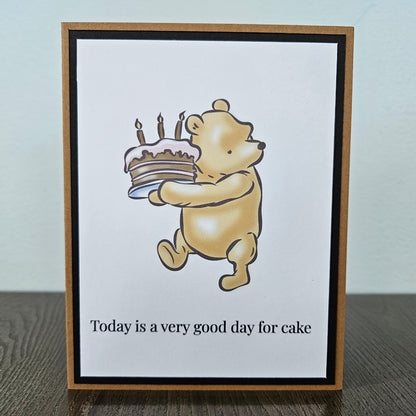 Card with a cartoon bear holding a cake and candles, with text 'Today is a very good day for cake'.