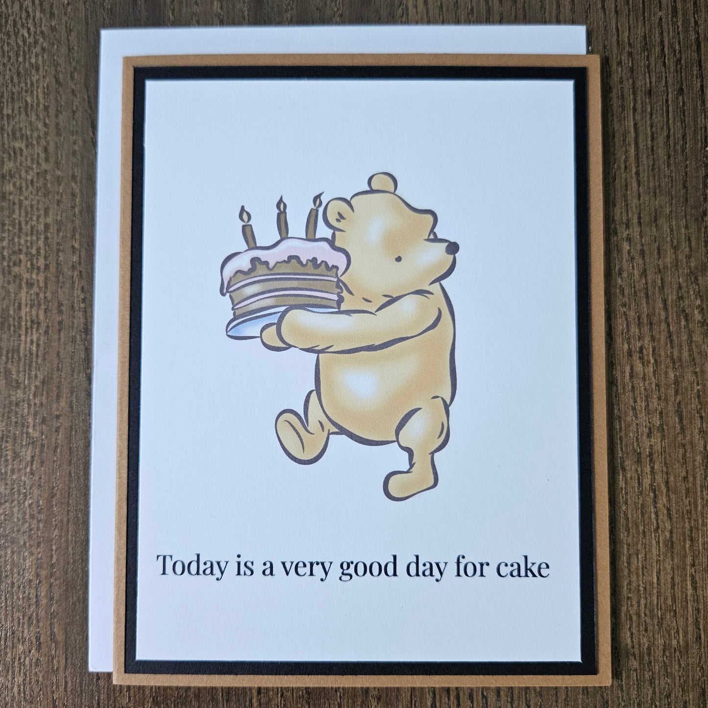Card with cartoon dog eating cake and text 'Today is a very good day for cake' on a wooden surface