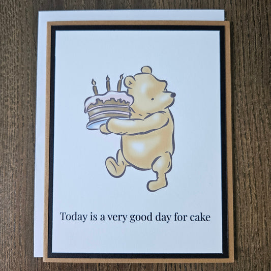 Card with cartoon dog eating cake and text 'Today is a very good day for cake' on a wooden surface