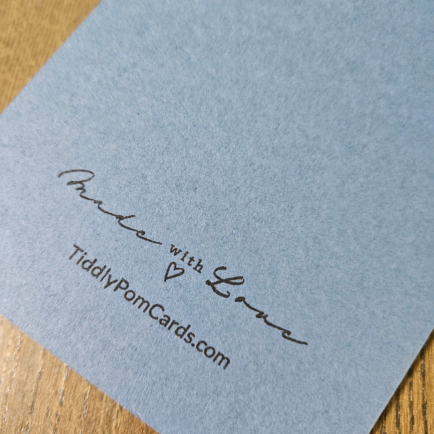 Blue card with 'Made with Love' and 'TiddlyPomCards.com' text on a wooden surface