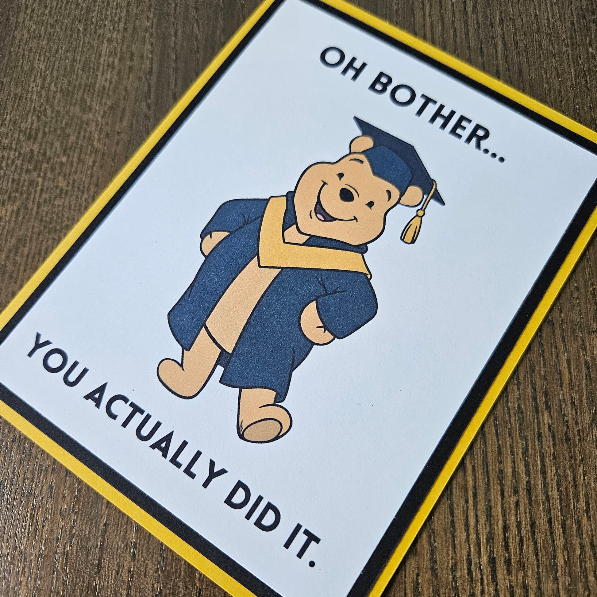Graduation-themed card with a bear in a cap and gown on a wooden surface
