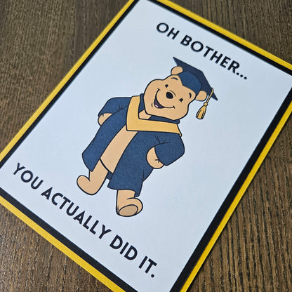 Graduation-themed card with a bear in a cap and gown on a wooden surface
